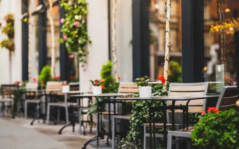 Mesas y sillas vacías en la terraza de un restaurante, adornadas con plantas y flores. Un lugar acogedor, listo para recibir clientes tras obtener las licencias de restaurantes.