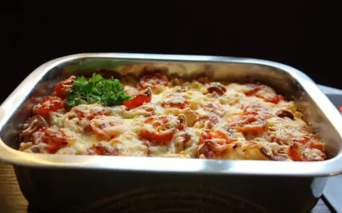 En gyllene makaronipudding med korv och tomater, toppad med smält ost och persilja. En klassisk svensk rätt som doftar hemlagat.