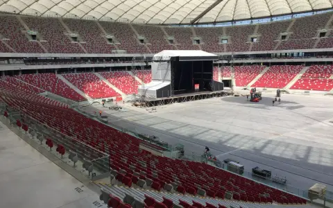 Przygotowania do koncertu Depeche Mode w Warszawie. Ogromny stadion z pustymi czerwonymi trybunami i sceną w budowie.