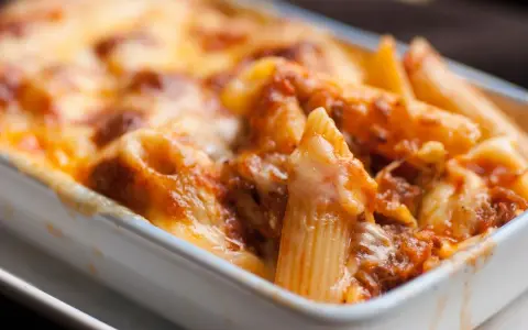 Piatto fumante di pasta pasticciata al forno, con penne ricoperte di sugo e formaggio fuso.