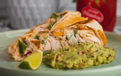 Roladka z tortilli z kurczakiem i warzywami, podana z guacamole i ćwiartką limonki. Idealny sos do tortilli!