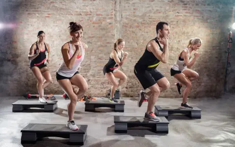 Un groupe de personnes participe à un cours step, effectuant des mouvements dynamiques sur des plateformes d'exercice dans une salle de sport.