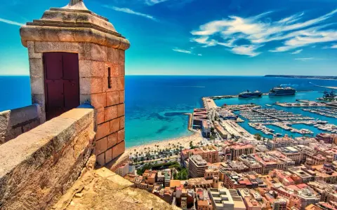 Alicante co zobaczyć: widok z zamku na port, plażę i miasto. W oddali statki wycieczkowe.