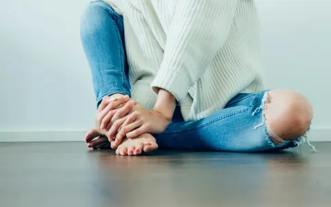 Frau mit zerrissener Jeans hält ihr Bein, das auf Schmerzen Knie Innenseite ohne Schwellung hindeutet.