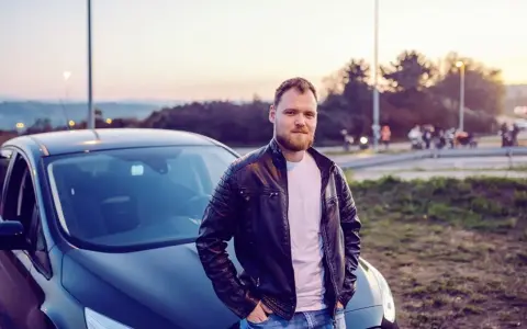 Mężczyzna w skórzanej kurtce opiera się o swój nowy samochód. To jego oc mubi, gotowy na przygodę.