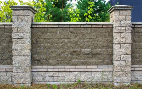 Solidne słupki ogrodzeniowe z betonu, obłożone kamieniem, tworzą elegancką całość z murem. Idealne rozwiązanie, czym obłożyć stare słupki ogrodzeniowe.