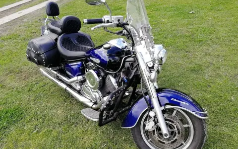 Błyszczący, niebieski motocykl Yamaha Drag Star 1100 z sakwami i dużą szybą, gotowy na podróż. Dane techniczne tego klasyka są imponujące.