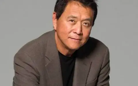 Robert Kiyosaki, autor "Bogatych ojców", w brązowej marynarce i czarnej koszulce, patrzy w obiektyw.