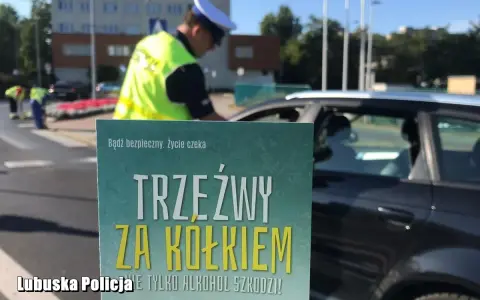 Policjant kontroluje kierowcę. Plakat informuje: "Trzeźwy za kółkiem". Co to znaczy trzeźwy? To bezpieczeństwo na drodze.