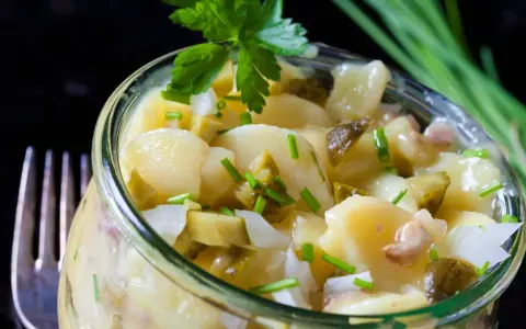 Ein köstlicher Kartoffelsalat ohne Mayo, mit Gurken und frischen Kräutern, serviert in einem Glas.