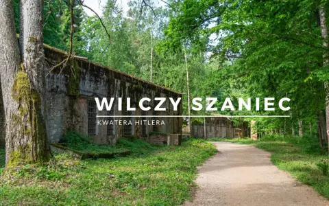 Wilczy Szaniec, dawna kwatera Hitlera, otoczona bujną zielenią. Kamienne mury i leśna ścieżka tworzą atmosferę minionych czasów.