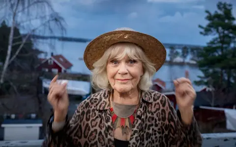 Christina Schollin, med sin karaktäristiska hatt och leopardmönstrade jacka, ser ut att berätta en historia från sina filmer och tv-program.