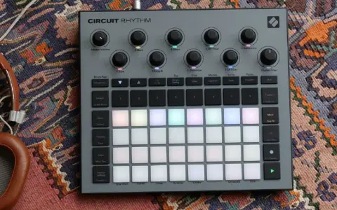 Szary kontroler Circuit Rhythm z podświetlanymi padami, gotowy do tworzenia muzyki. Słuchawki obok dopełniają scenę.