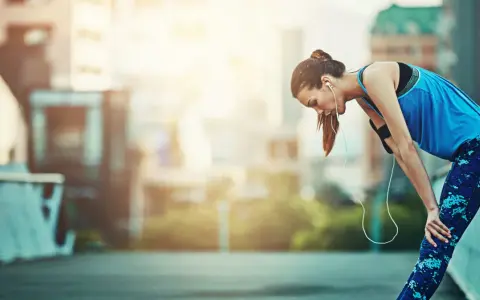 Atleta esausta appoggiata a un corrimano, con le cuffie. Potrebbe aver bisogno di rimedi per il sovrallenamento.
