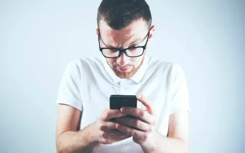 Zastanawiasz się, skąd firma windykacyjna ma Twój numer telefonu? Mężczyzna w okularach patrzy zdezorientowany na ekran smartfona.