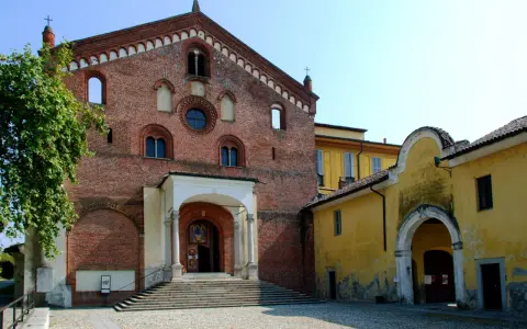 Morimondo cosa vedere: imponente facciata in mattoni rossi di un'antica abbazia, con scalinata e portico. Accanto, un edificio giallo con un arco.