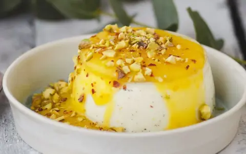 Budino fatto in casa cremoso, con salsa gialla e granella di pistacchi, servito in una ciotola bianca.