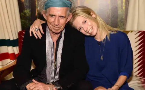 Keith Richards och en ung kvinna ler mot kameran. Hon vilar huvudet mot hans axel.