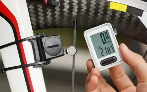 Rowerzysta sprawdza licznik pokazujący dystans 21.87 km. Obok widoczny czujnik na kole, który mierzy obwód koła rowerowego.