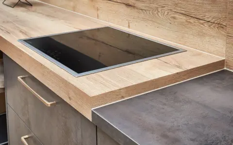Eine moderne Küche mit einer Holzoptik-Arbeitsplatte und einem dunklen Stein-Arbeitsplatten-Material. Ein Kochfeld ist eingelassen.