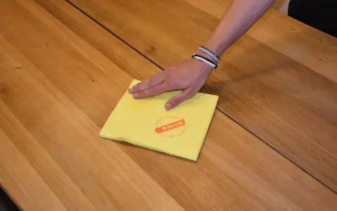 Hand wischt mit gelbem Tuch über Holzoberfläche, um den holztisch aufhellen.