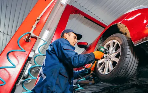 Mechaniker wechselt Reifen an rotem Auto. Informieren Sie sich, was kostet reifenwechsel, um Ihr Fahrzeug sicher zu halten.