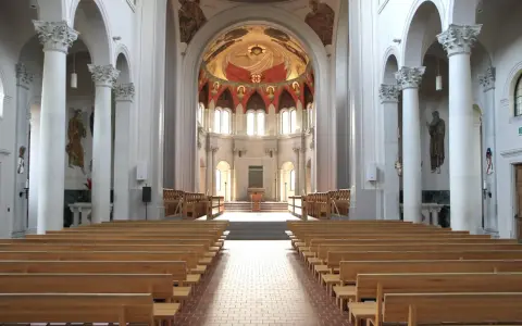 Interior of a grand abbey, with rows of wooden pews leading to an altar. The domed ceiling features a vibrant fresco. Check the abbey mass schedule for service times.