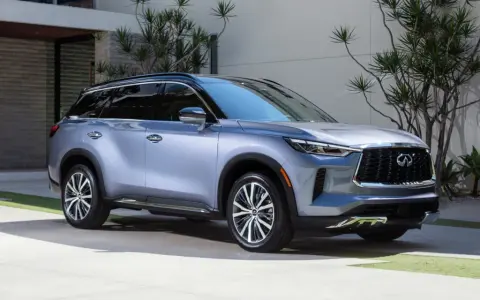 Elegancki, srebrny Infiniti SUV zaparkowany przed nowoczesnym domem z bujną roślinnością.
