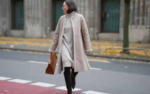 A woman demonstrates how to layer a dress for winter with a cozy turtleneck dress, a shearling coat, and stylish boots.