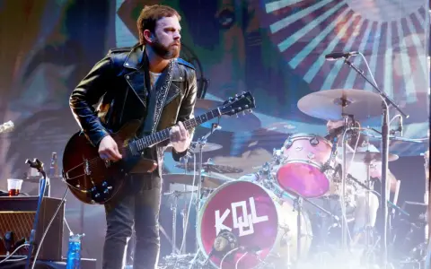 Gitarzysta Kings of Leon Polska w skórzanej kurtce gra na scenie. W tle perkusja z logo KQL.