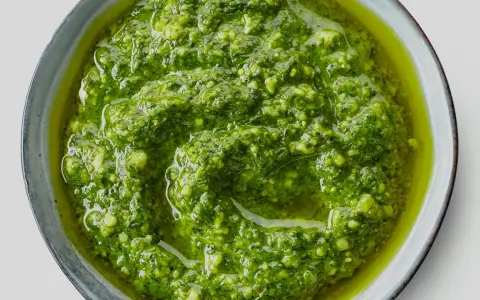 Närbild på hemmagjord pesto i en skål. Oljan flyter runt den gröna, grovhackade peston. Perfekt för att förlänga hållbarheten.