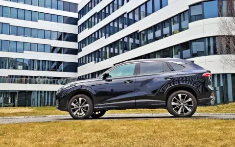 Czarny SUV MG HS, z nowoczesnym designem, zaparkowany przed biurowcem. Jego linia nadwozia sugeruje dynamiczne osiągi i niskie spalanie.