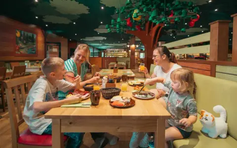 Familie genießt ein fröhliches Frühstück in einem fantasievollen Legoland Restaurant mit Baumdeko.