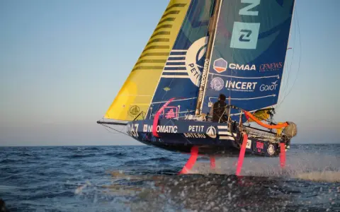 Segelboot mit pinken Foils rast über die Wellen. Ein Skipper steuert das Boot bei der Mini Transat Regatta.