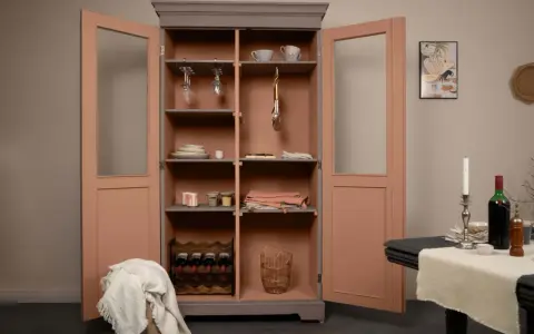 Armoire vitrée avec un relooking meuble 2 couleurs : gris anthracite et rose poudré. Elle contient vaisselle, verres, bouteilles de vin et objets déco.