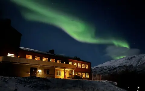 Norrsken över ett snötäckt landskap med ett hus. Perfekt för kiruna sightseeing turer.