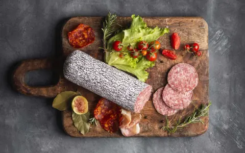Assortimento di tipi di salame su tagliere in legno, con pomodorini, lattuga e fichi.