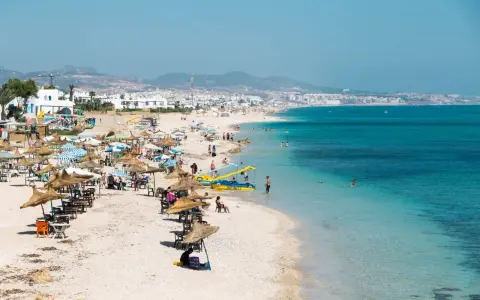 Spiaggia affollata in Marocco con bambini che giocano in acqua e famiglie che si rilassano sotto gli ombrelloni.