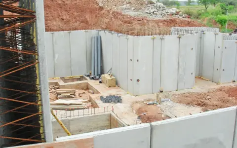 Construcción de un muro de contención con paneles prefabricados de hormigón. Se observan tuberías y materiales de construcción en el sitio.