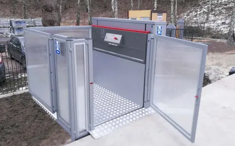 Nowoczesny dźwig dla niepełnosprawnych, z drzwiami otwieranymi na zewnątrz, ułatwia dostęp do budynku.