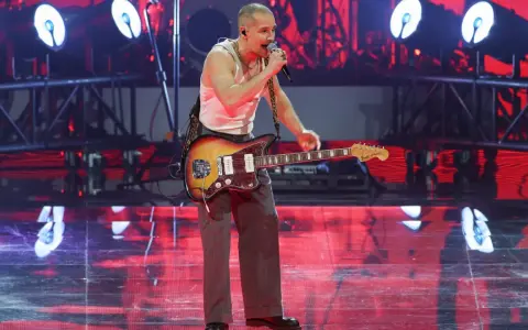 Krzysztof Zalewski na koncercie, śpiewa i gra na gitarze. Scena oświetlona czerwonymi światłami.