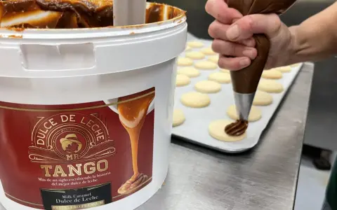 Un repostero decora galletas con una manga pastelera, usando el delicioso dulce de leche de un gran envase.