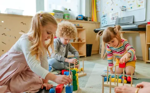 Drei Kinder, darunter ein **kind 8 jahre**, spielen konzentriert mit bunten Holzbausteinen im Kindergarten.