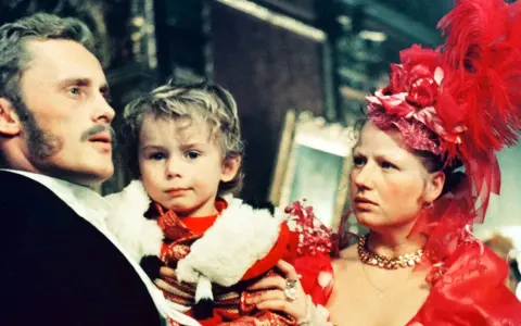 Rodzina w bogatych strojach, ojciec trzyma dziecko. Scena z filmu "Ziemia obiecana" streszczenie.
