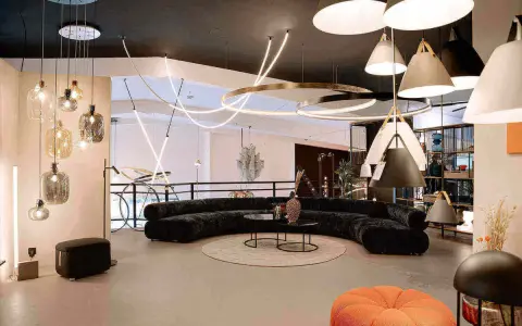 Un salon moderne avec un canapé incurvé noir, des tables basses, un tapis rond et une variété d'ampoules design suspendues au plafond.