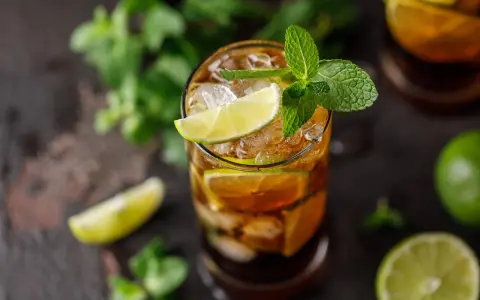 Szklanka z drinkiem Cuba Libre, lodem, plasterkami limonki i miętą.