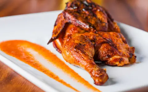 Un délicieux poulet portugais au four, la peau dorée et croustillante, servi avec une sauce épicée sur une assiette blanche.