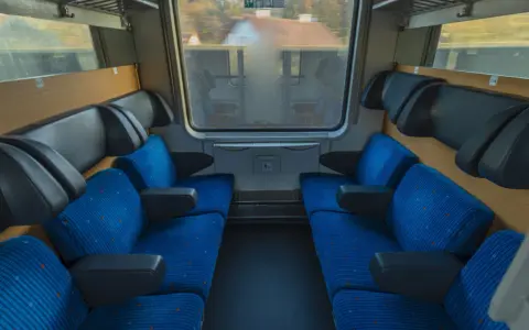 Leere Sitze im Nachtzug nach Stockholm. Blaue Polster mit orangefarbenen Punkten und schwarze Armlehnen laden zur Reise ein.