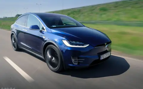 Granatowy Tesla Model X w ruchu na drodze, z widocznym kierowcą.