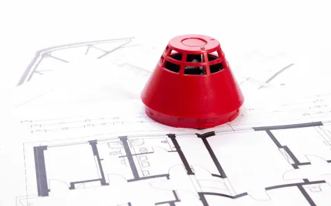 Roter Rauchmelder auf Bauplänen. Ein Beispiel für baulichen Brandschutz, der Sicherheit in Gebäuden gewährleistet.
